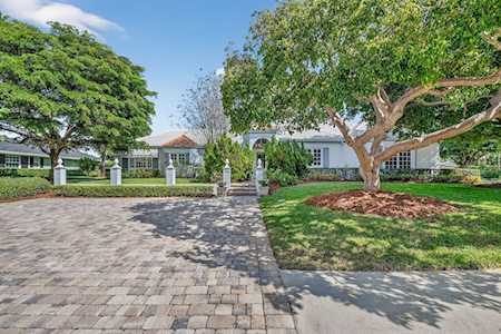 Single-story white home behind a paved driveway, framed by mature trees and a front lawn.