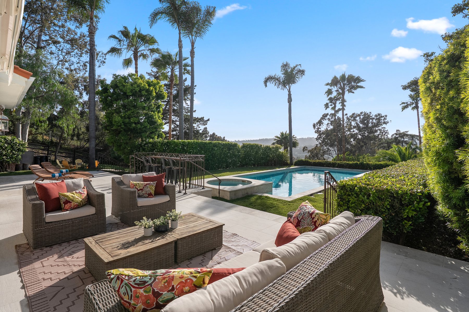 Furnished patio overlooking a swimming pool and spa, framed by palms and distant hills.