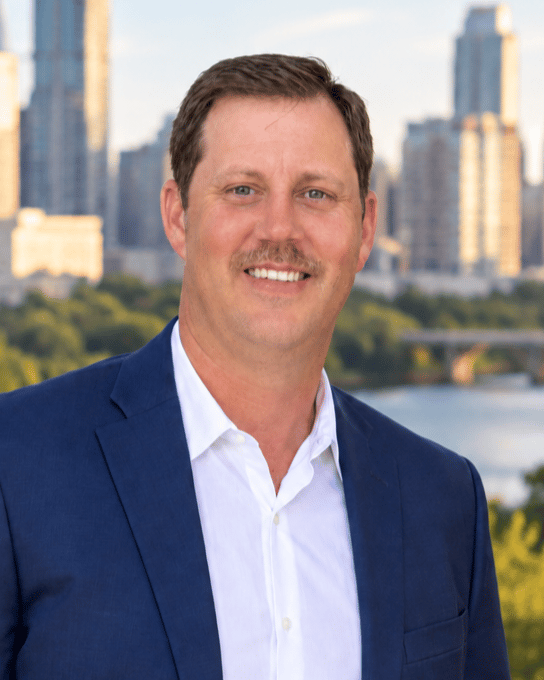Jeff Marischen wearing a navy blazer and white shirt, with a city skyline behind him.