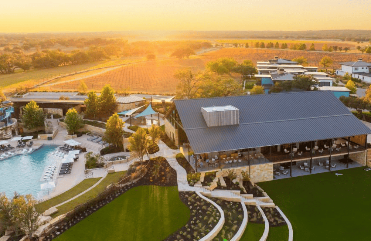 Aerial view of a stone clubhouse and pool amid landscaped grounds and autumn countryside.