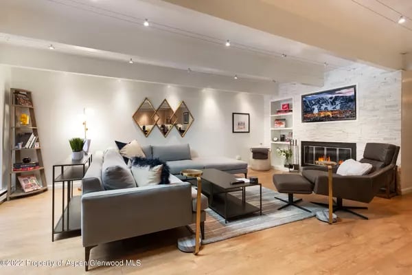 Living room with a gray sectional, hardwood floors, and a white stone fireplace.
