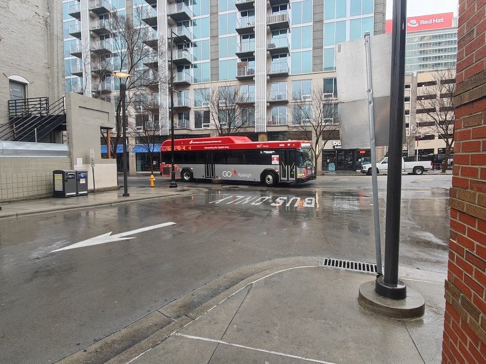 A city street scene featuring a bus turning at an intersection, with nearby buildings and wet pavement.