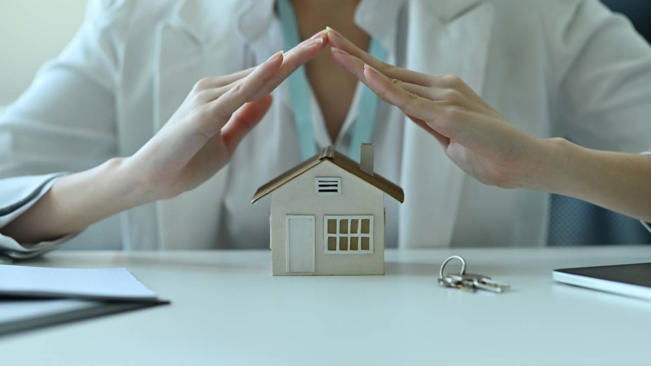 Hands forming a roof over a small house model on a desk, symbolizing home expenses and the Aspen CO cost of living in today’s market.