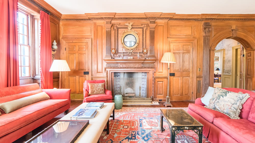 Living room with carved wood paneling, a marble fireplace, red sofas, and a patterned rug.