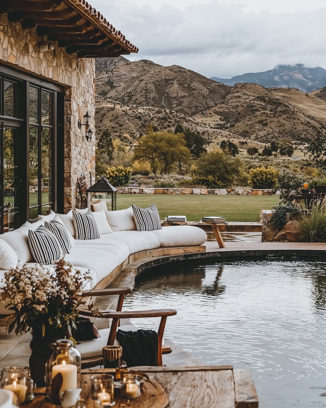 Luxury stone home with mountain view, outdoor lounge seating, and reflection pool surrounded by neutral décor