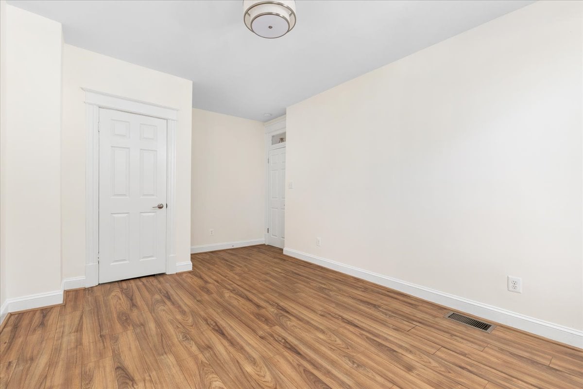 Empty room with wood-look flooring, white paneled doors, and a ceiling light.