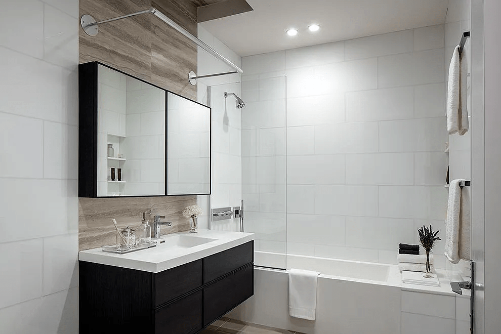 Modern bathroom with a dark vanity, mirrored cabinet, and white tiled tub and shower.