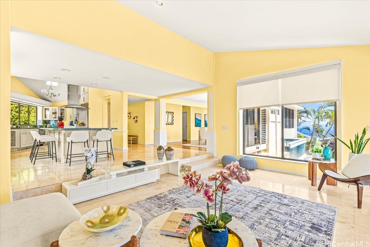 Living room with an open kitchen, yellow walls, and a large window overlooking palm trees and water.