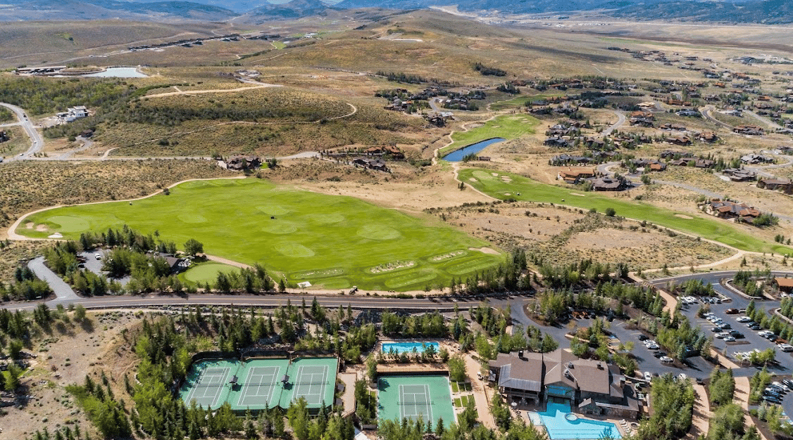 Aerial view of a hillside community with a golf course, tennis courts, clubhouse, and pool.