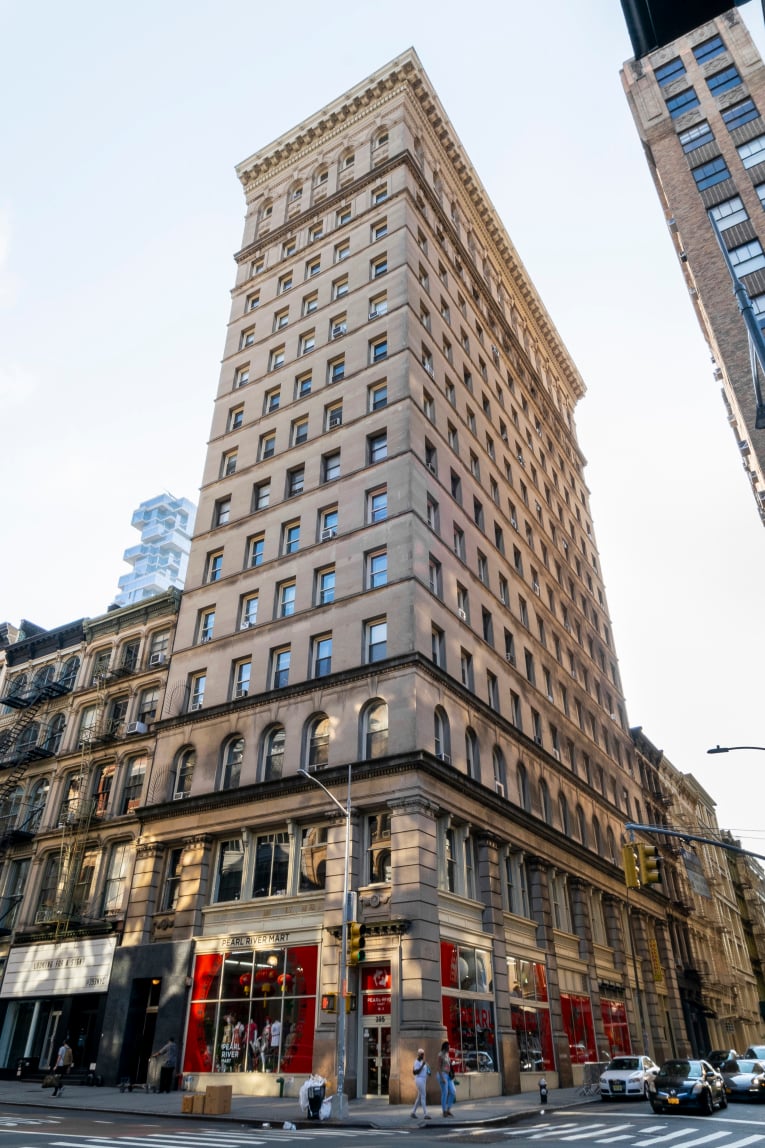 Tall stone building with an ornate cornice and Pearl River Mart storefronts on the corner.