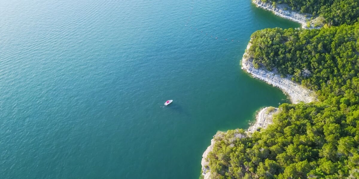 Pristine Lake Austin waters with recreational boat surrounded by protected Hill Country landscape, demonstrating the natural beauty of Austin's luxury waterfront living