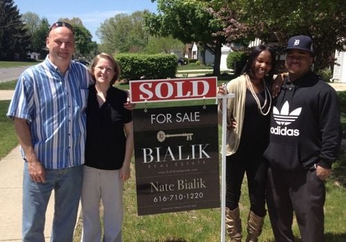 Four adults pose beside a Bialik Real Estate sold sign.