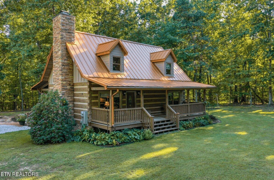 Rustic log cabin with a copper-colored roof and covered porch among trees.