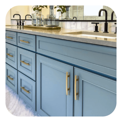 Bathroom vanity with blue cabinets, brass pulls, and a pale veined stone countertop.