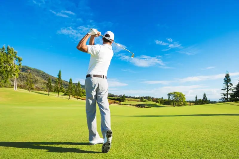 Golfer taking a swing on a sunny day at a scenic golf course near Aspen with green fairways and clear blue skies.