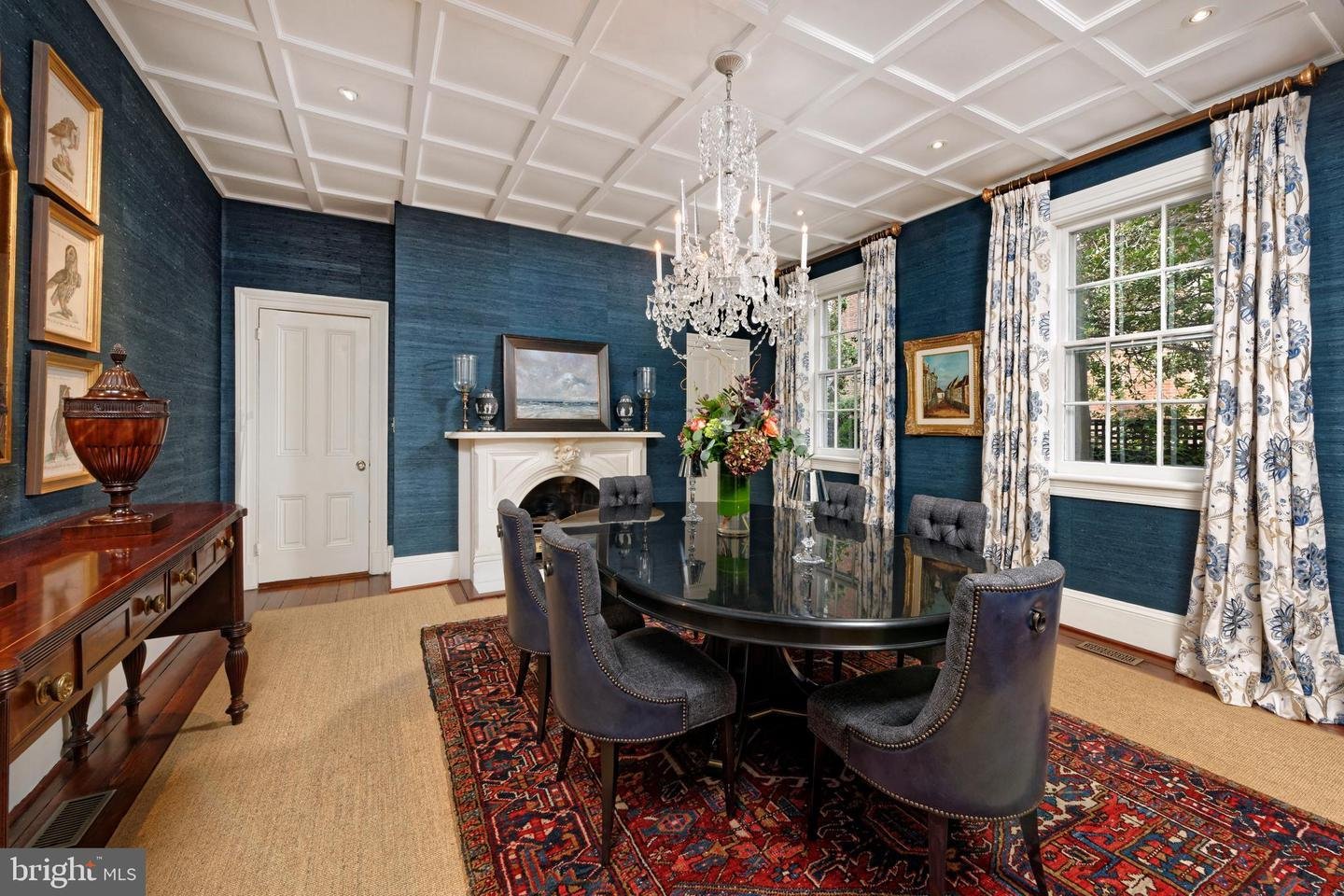 Dining room with deep blue walls, a coffered ceiling, crystal chandelier, and oval table with upholstered chairs.