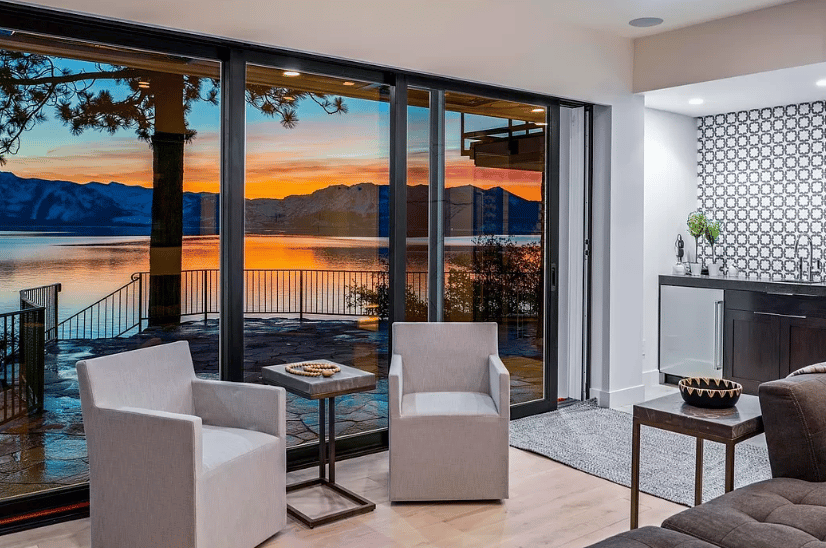 Modern living room with floor-to-ceiling glass doors overlooking Lake Tahoe at sunset.