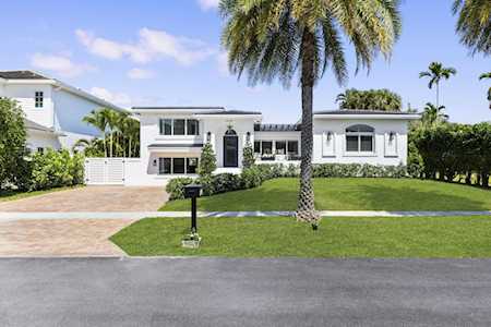 Modern white single-story house with a wide lawn, paved driveway, and tall palm tree.