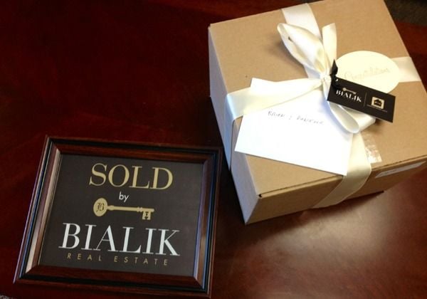 Bialik Real Estate SOLD plaque beside a white-ribboned gift box.
