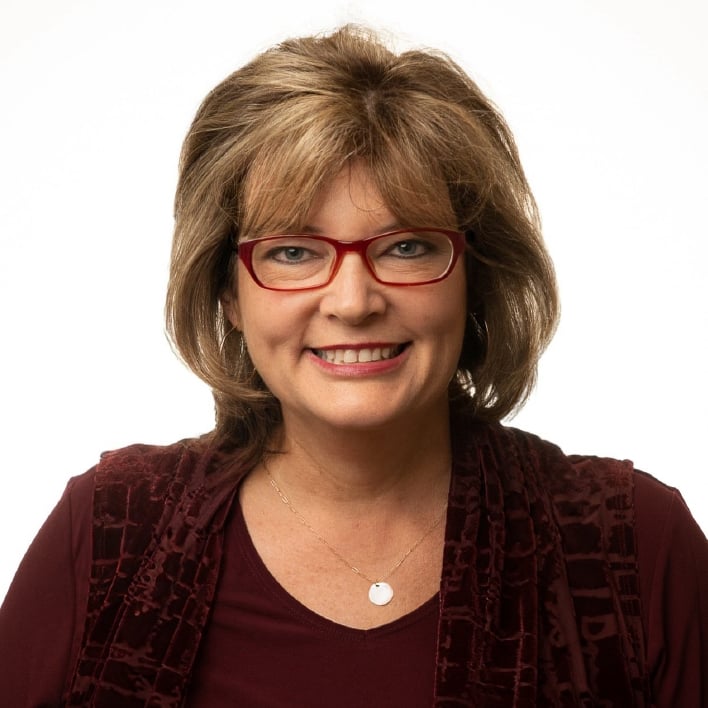 Smiling woman with red glasses and shoulder-length brown hair.