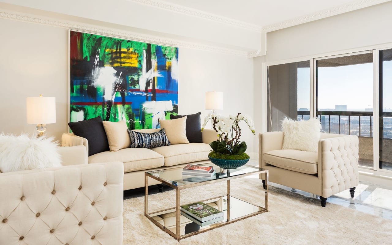 Comfortable living room featuring plush white sofas, a soft rug, and a large, vibrant painting, creating an inviting space.