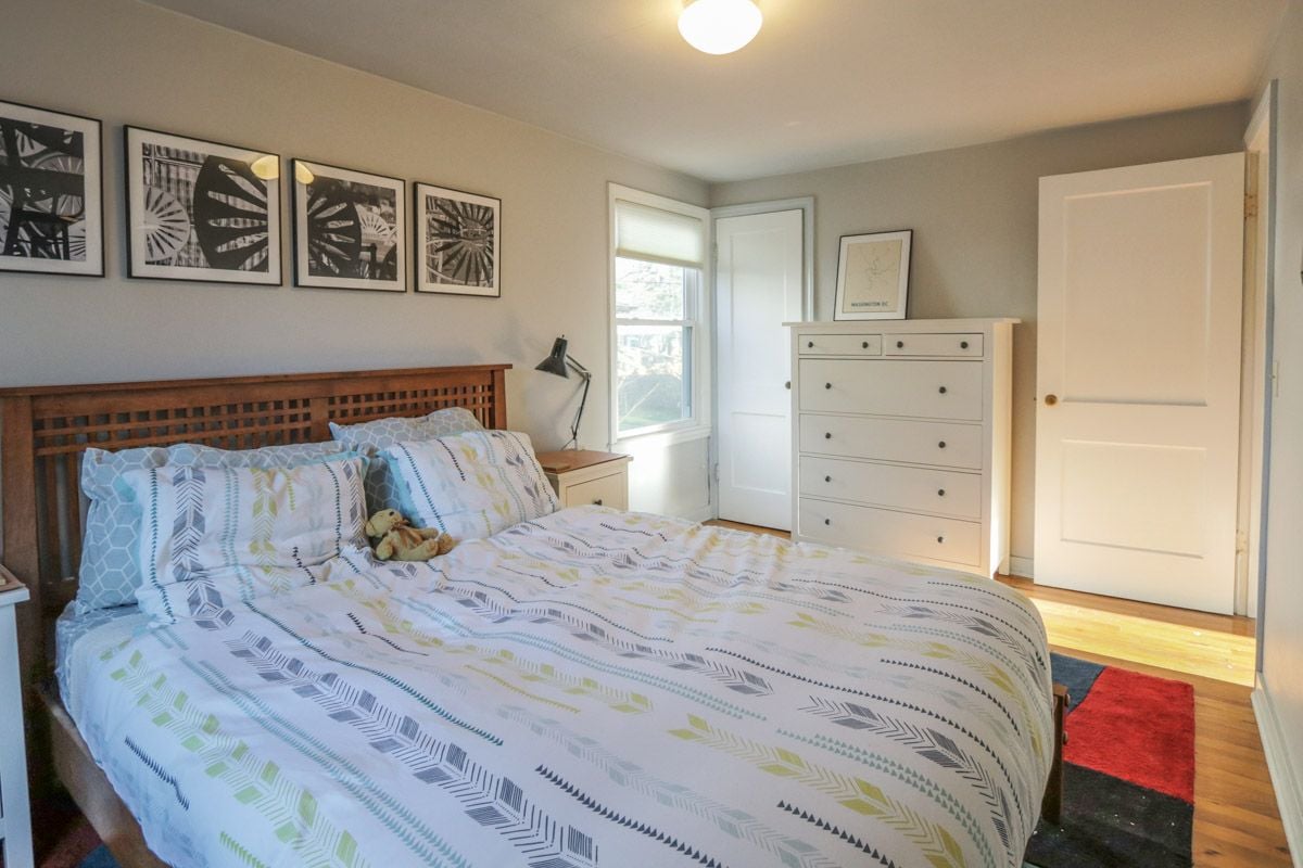 Furnished bedroom with patterned bedding, a dark wood headboard, and a white dresser.