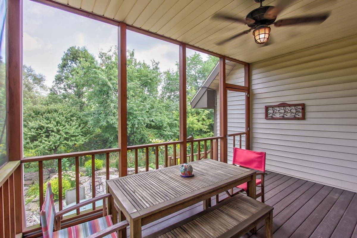 Screened porch with a wooden dining set, ceiling fan, and leafy garden views.