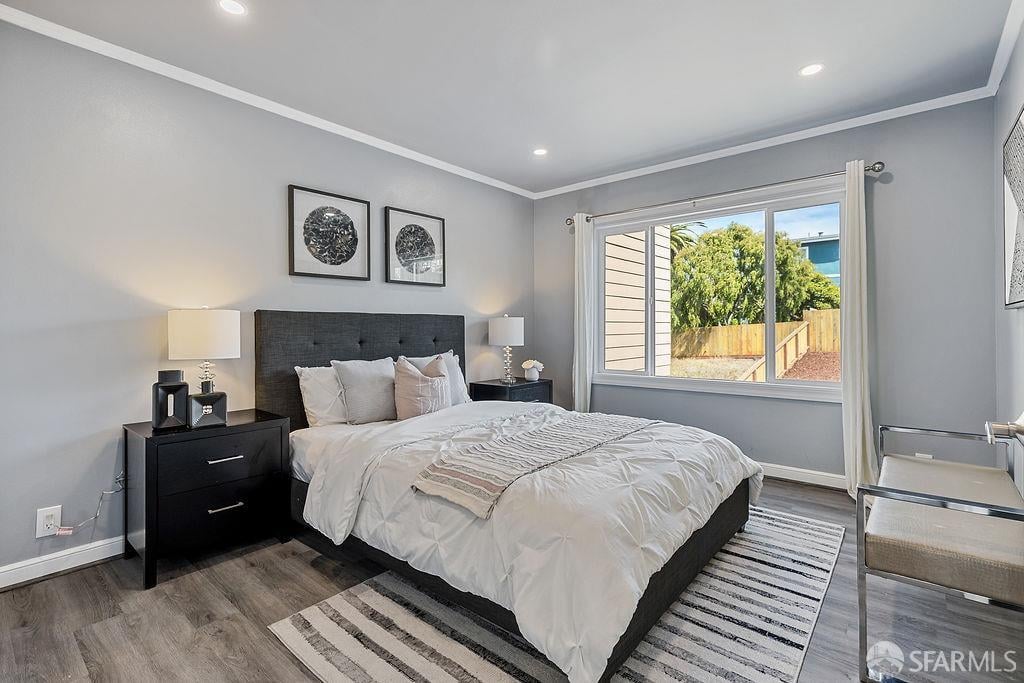 Furnished bedroom with a dark upholstered bed, white bedding, and a large window overlooking a fenced yard.