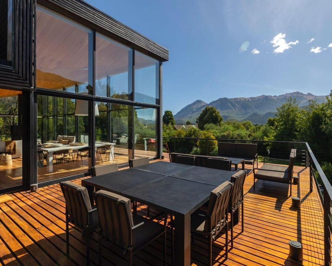 Furnished wooden deck with outdoor dining table and lounge seating overlooking trees and mountains.