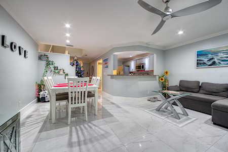 Open-plan living and dining area with a gray sectional, glass coffee table, and white dining set.
