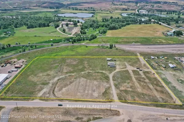 Aerial view of an undeveloped parcel outlined in yellow beside a road and rural fields.