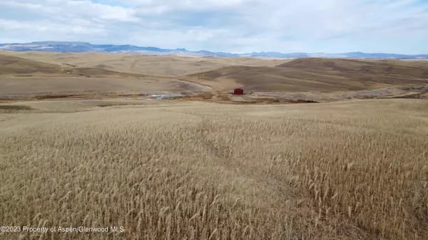 Golden field and rolling hills with a small red barn and distant mountain ridges.