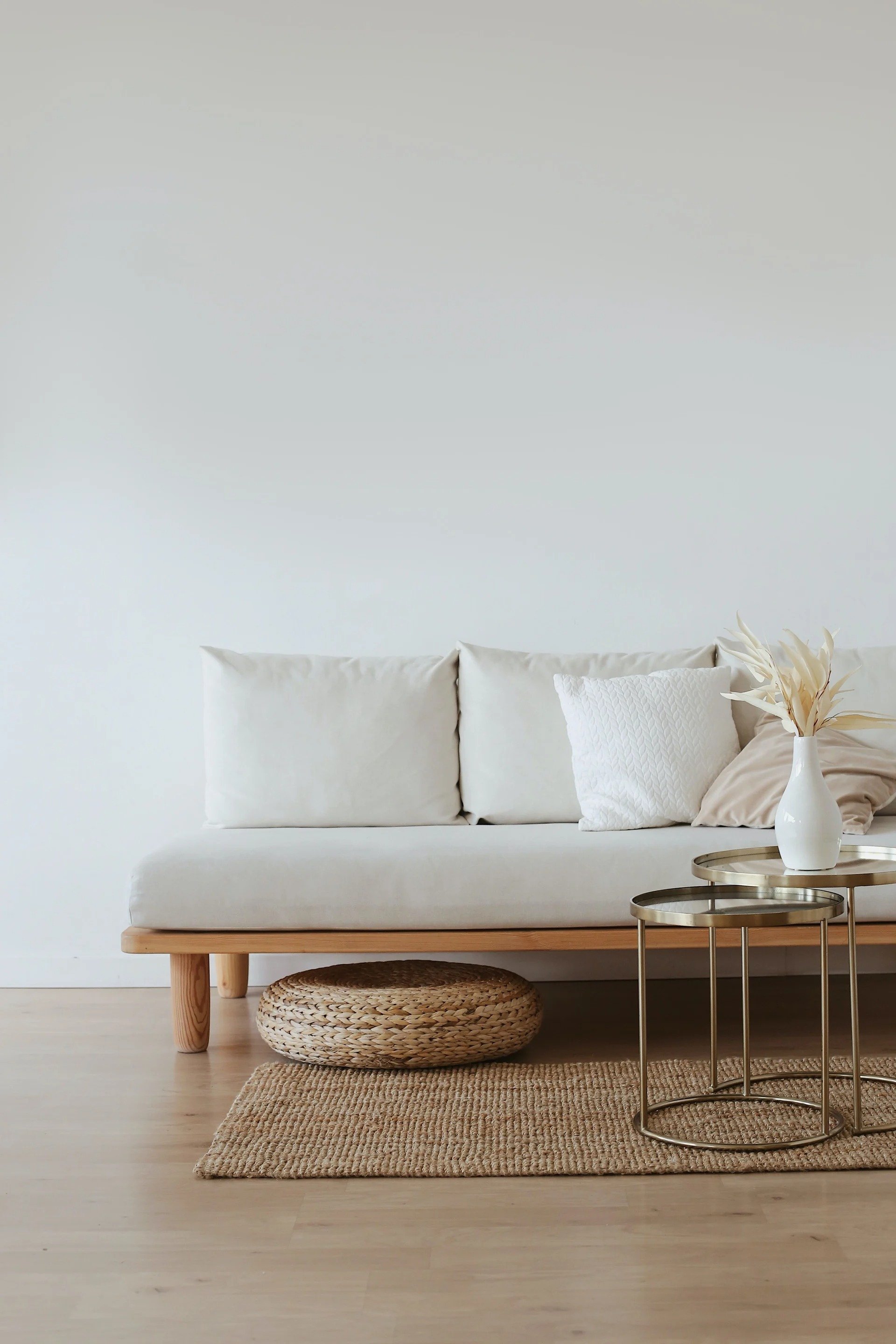 Cream sofa with textured pillows, woven pouf, jute rug, and gold nesting tables in a minimalist living room.