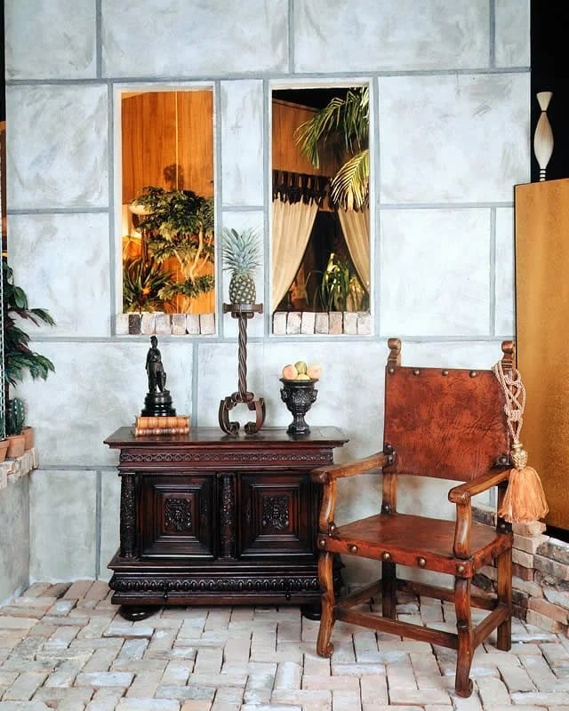 A furnished set with a carved dark cabinet, leather chair, and plant-filled faux windows.