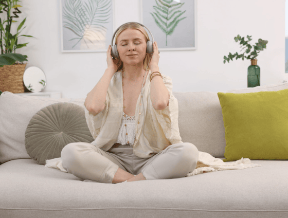 Woman relaxing on a sofa with headphones, eyes closed, in a bright living room.