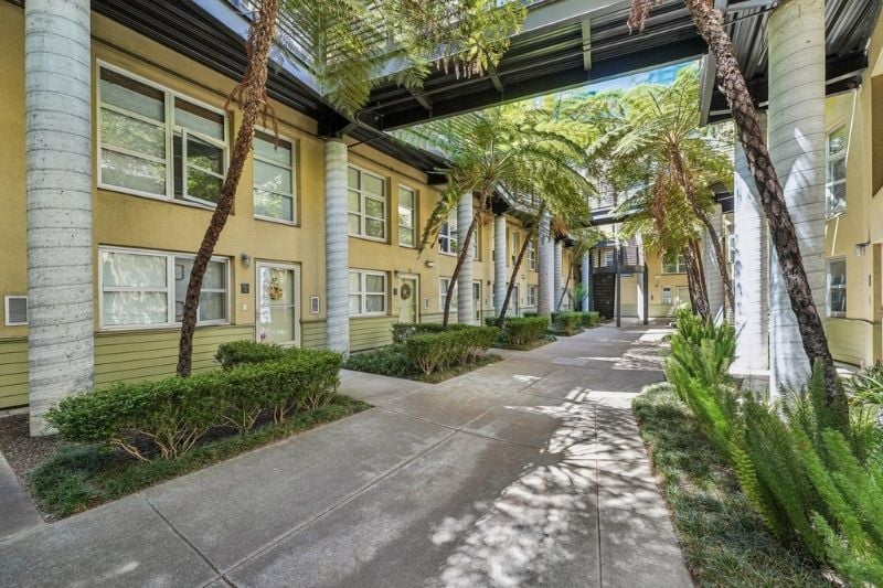 A perspective shot of the courtyard at Harbor Lofts, showcasing the walkway, green foliage, and the overhead structure connecting the buildings.