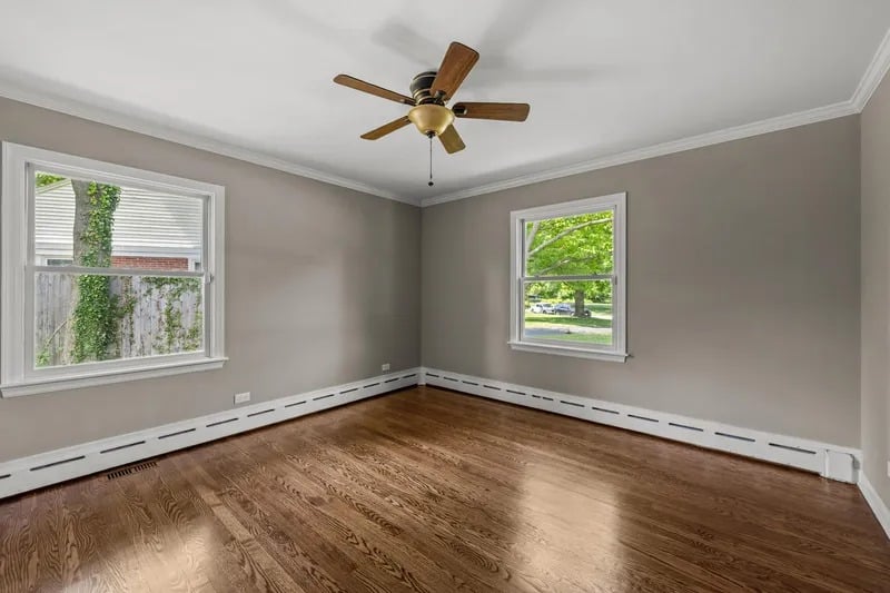 Empty room with hardwood floors, gray walls, two windows, and a ceiling fan.