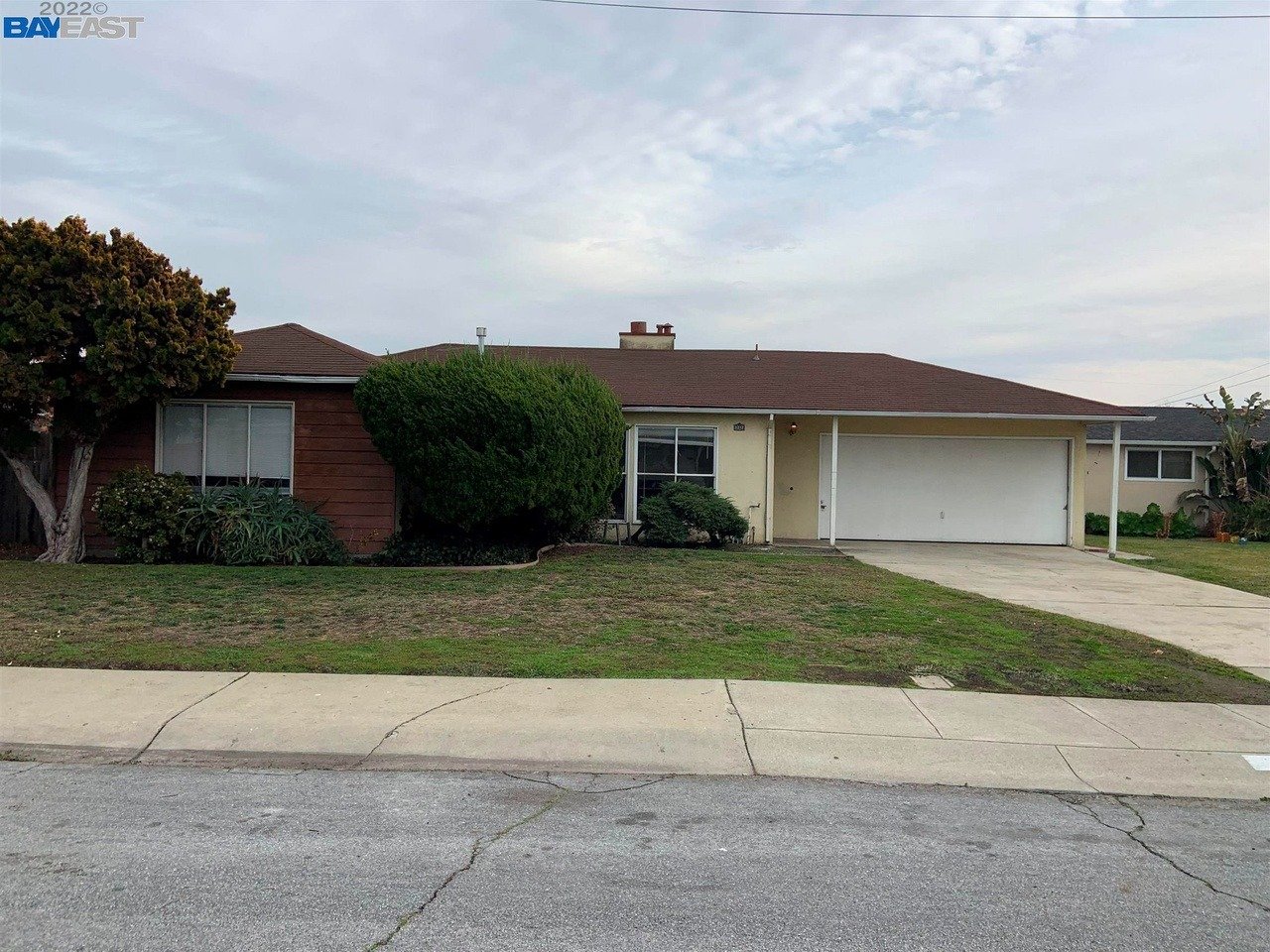 Single-story house with brown siding, an attached garage, and a broad front lawn.