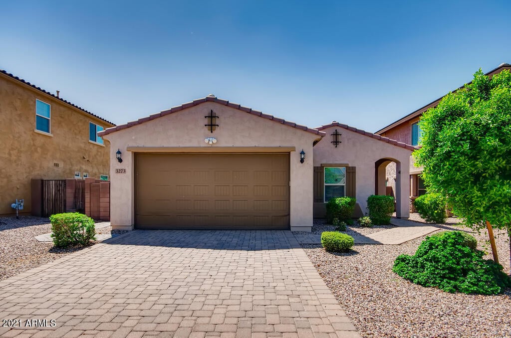 Single-story stucco home with a wide garage, paver driveway, and gravel landscaping.