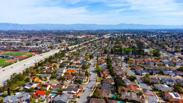 Aerial view of a residential neighborhood beside a highway, with sports fields and distant hills.
