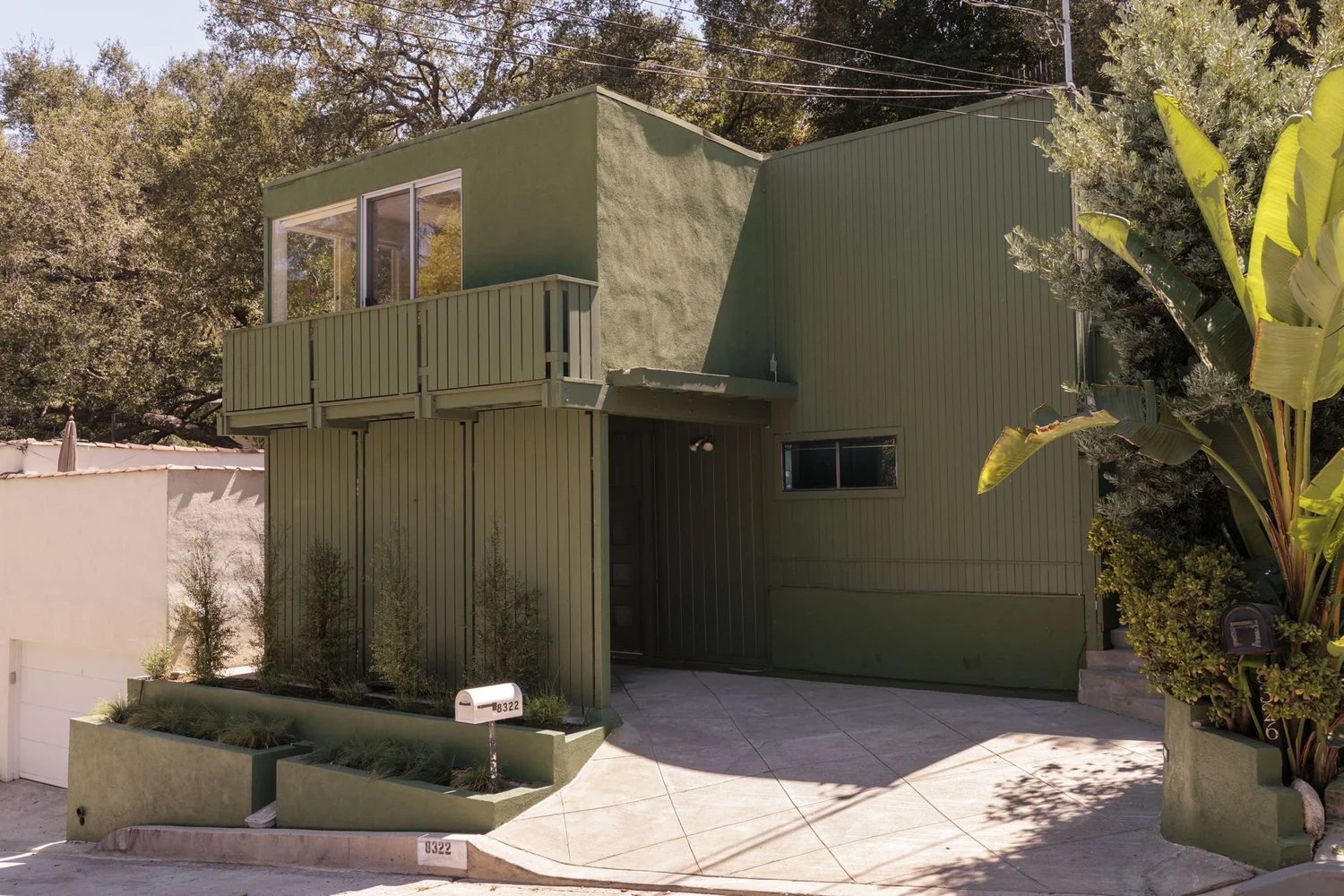 The Margaret O. Smith Residence from the street: a two-level house clad in green-painted vertical board siding, with a glassy upper level and balcony set among canyon oaks.