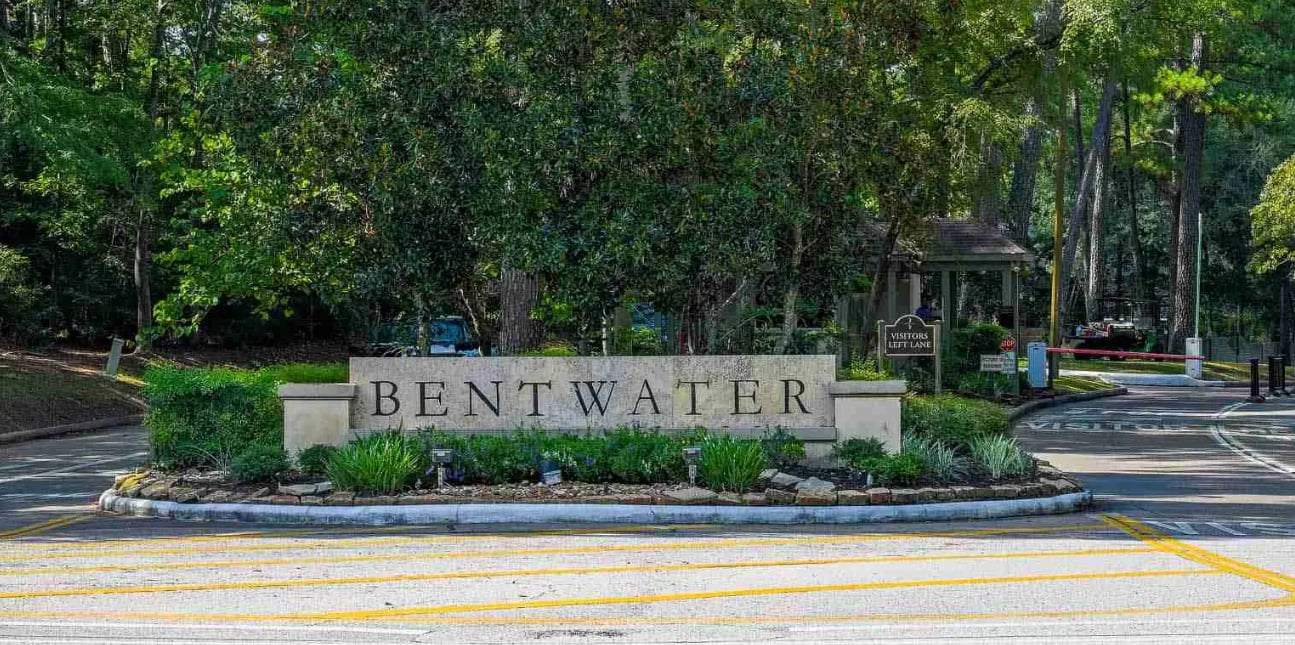 Bentwater entrance sign beside a gated roadway, surrounded by mature trees and landscaping.