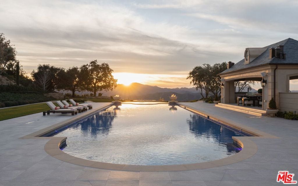 Swimming pool and stone terrace with loungers, outdoor dining, and mountain views at sunset.