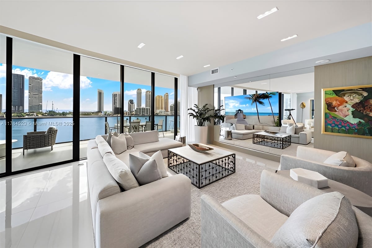 Prive Island living room with white sofas, floor-to-ceiling windows, and waterfront city views.