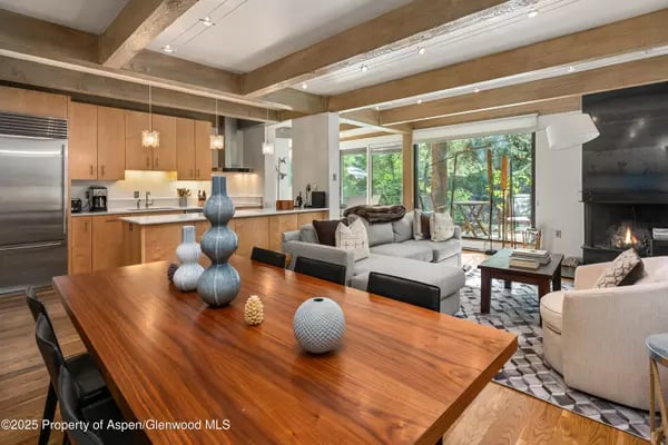 Open-plan home with wood ceiling beams, a dining table, kitchen, and living room fireplace.