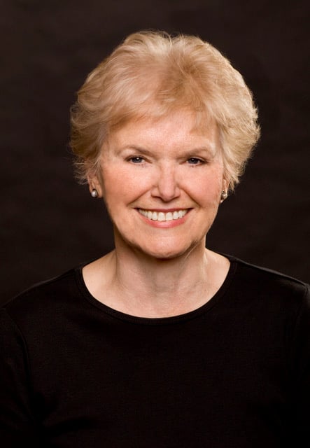 Joan O'Connell smiling in a black top against a dark background.
