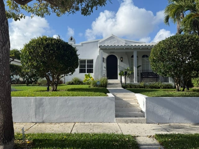 White home with an arched entry, covered porch, and steps through a landscaped front yard.