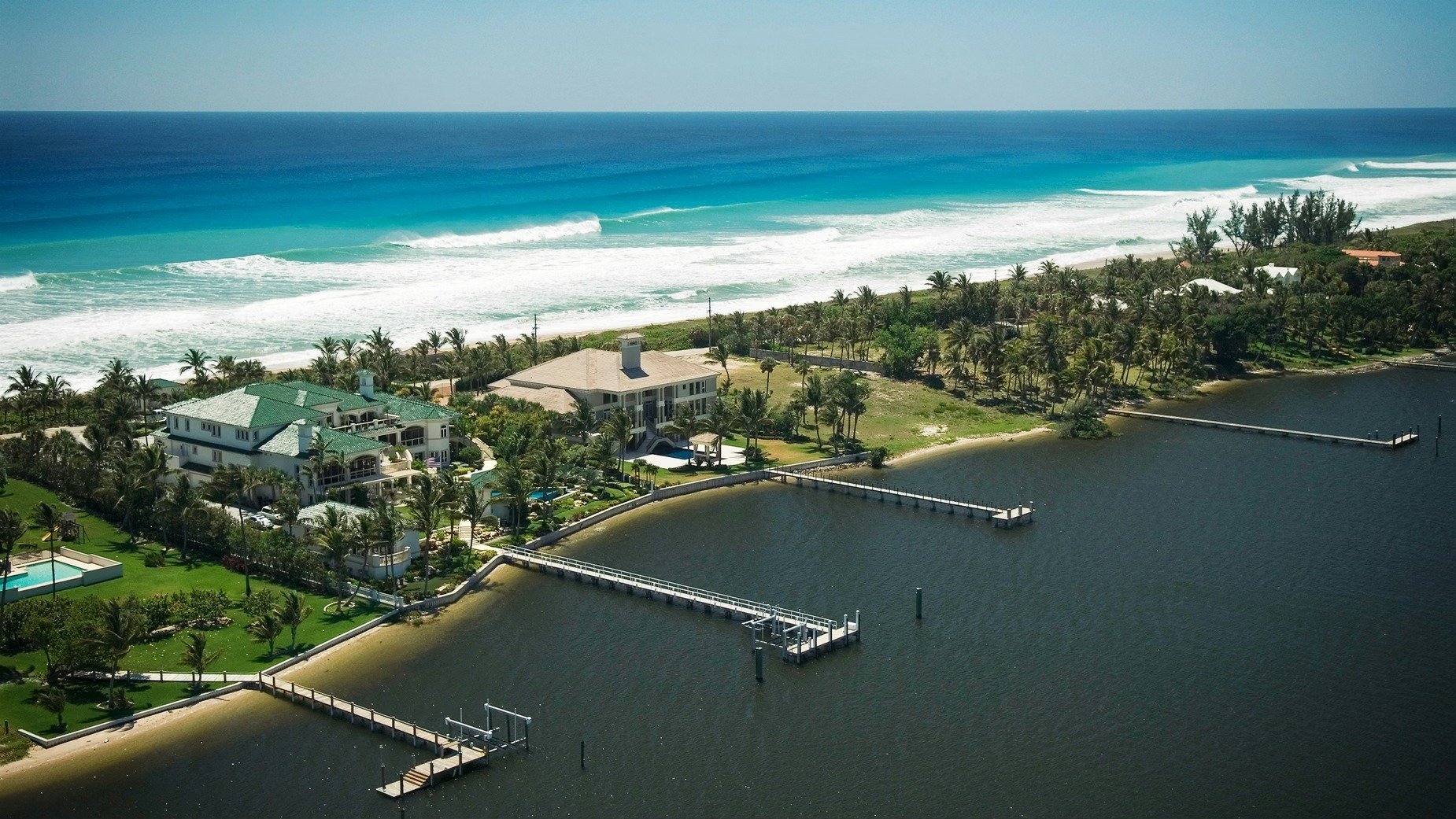 Aerial view of waterfront estates between ocean and lagoon, with private docks and palm-lined grounds.