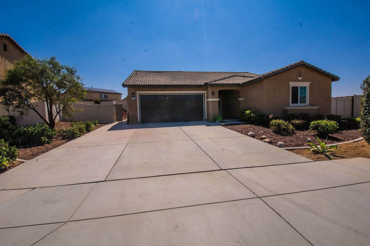 Single-story tan house with a two-car garage, wide driveway, and landscaped front yard.