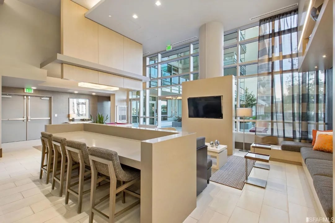 Arden Residences lounge with a long bar table and stools next to a TV.